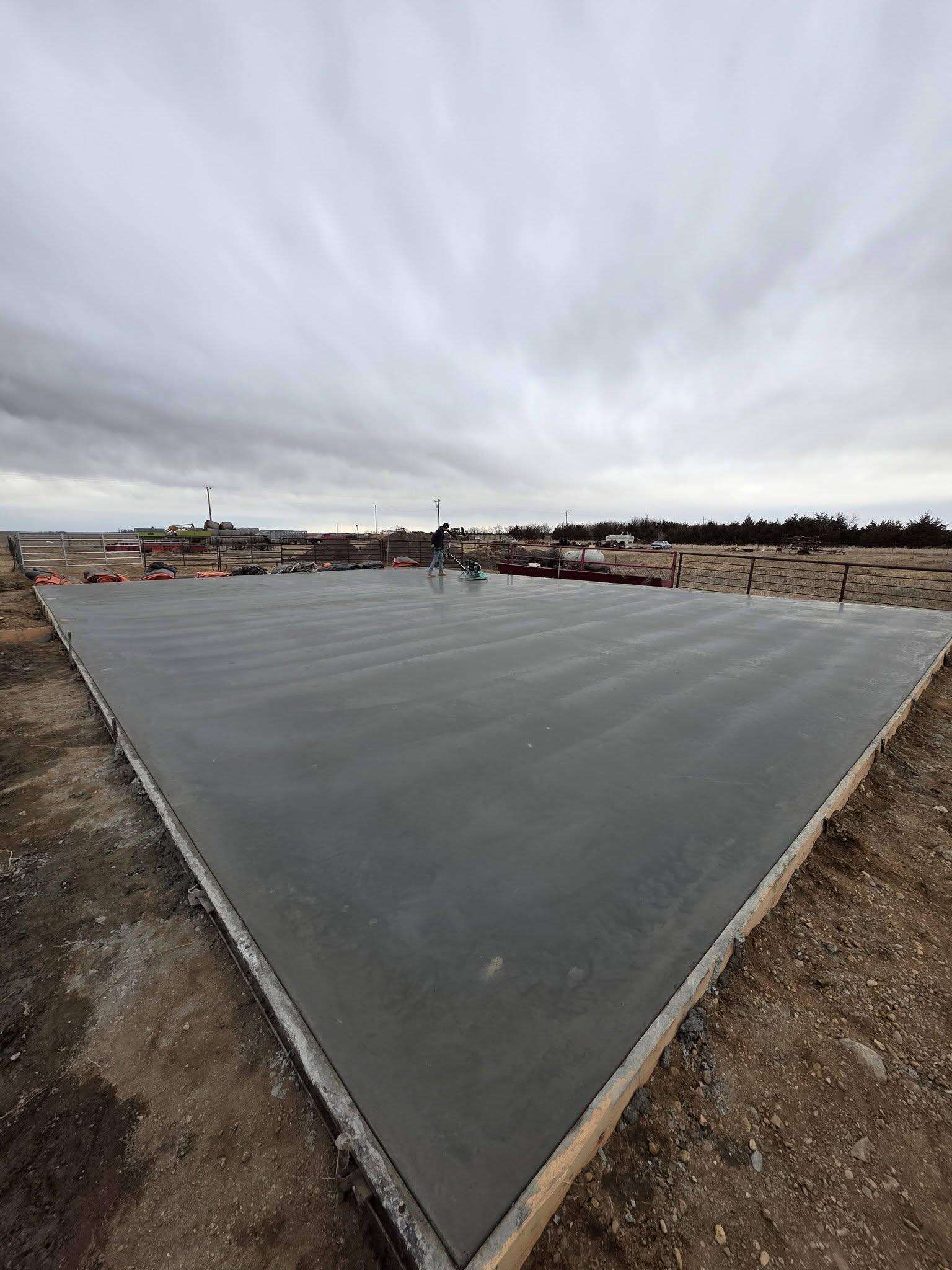 A large finished ag building pad, machine-troweled flat, edge-on under a prairie sky