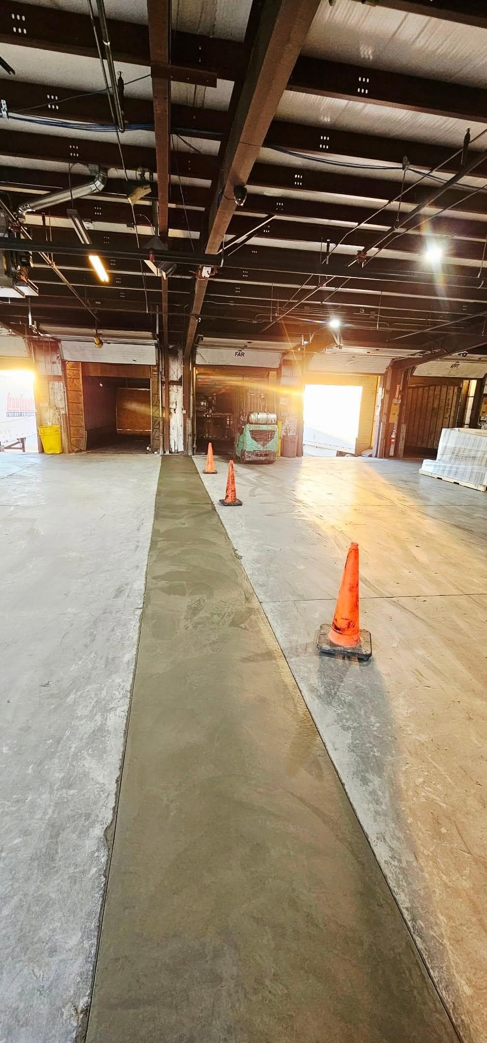 A new concrete strip poured through an existing warehouse floor, cones down the run