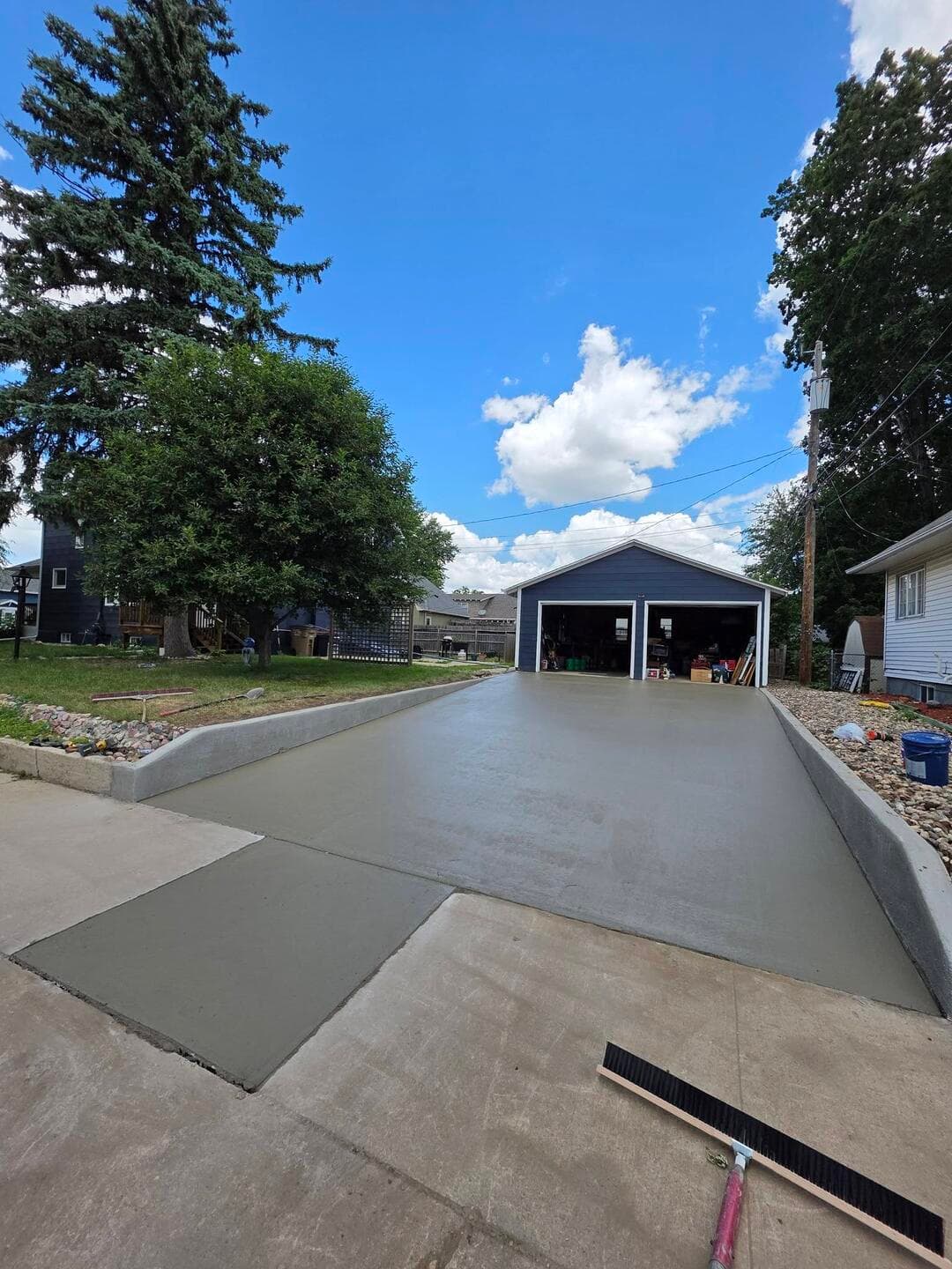 A wide fresh driveway and new apron poured beside an existing walk, screed board still at the edge