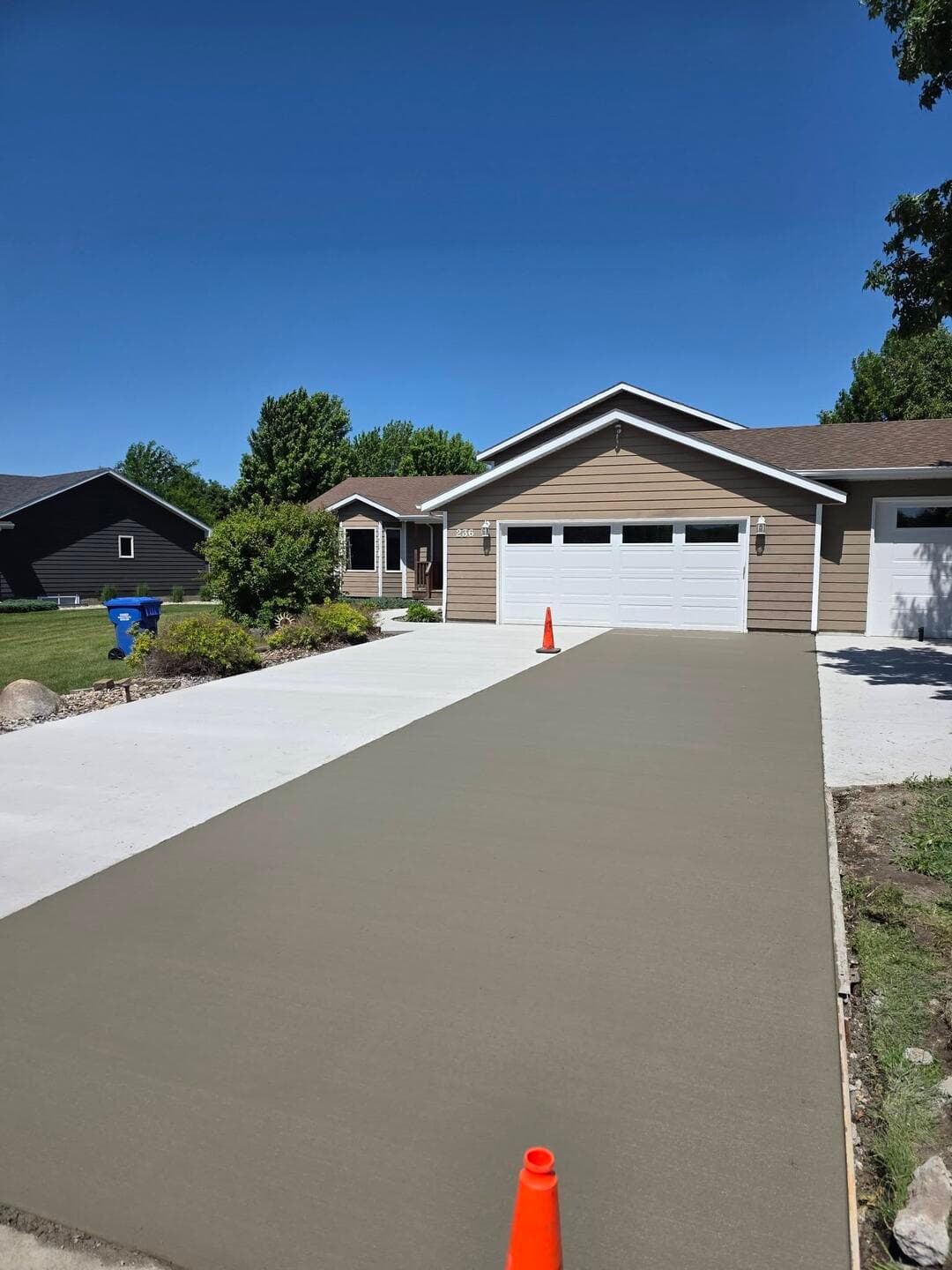 A fresh gray broom-finished driveway with a cone still set at a tan home