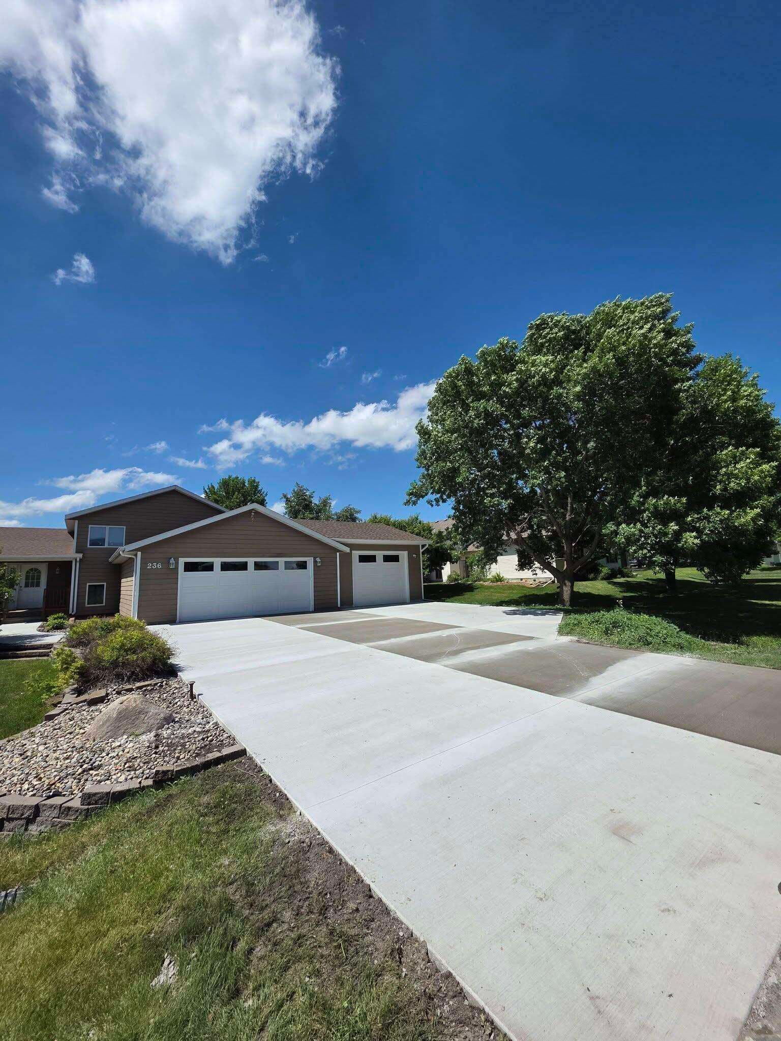 A long, freshly finished concrete driveway running from the street to a detached garage under a blue sky