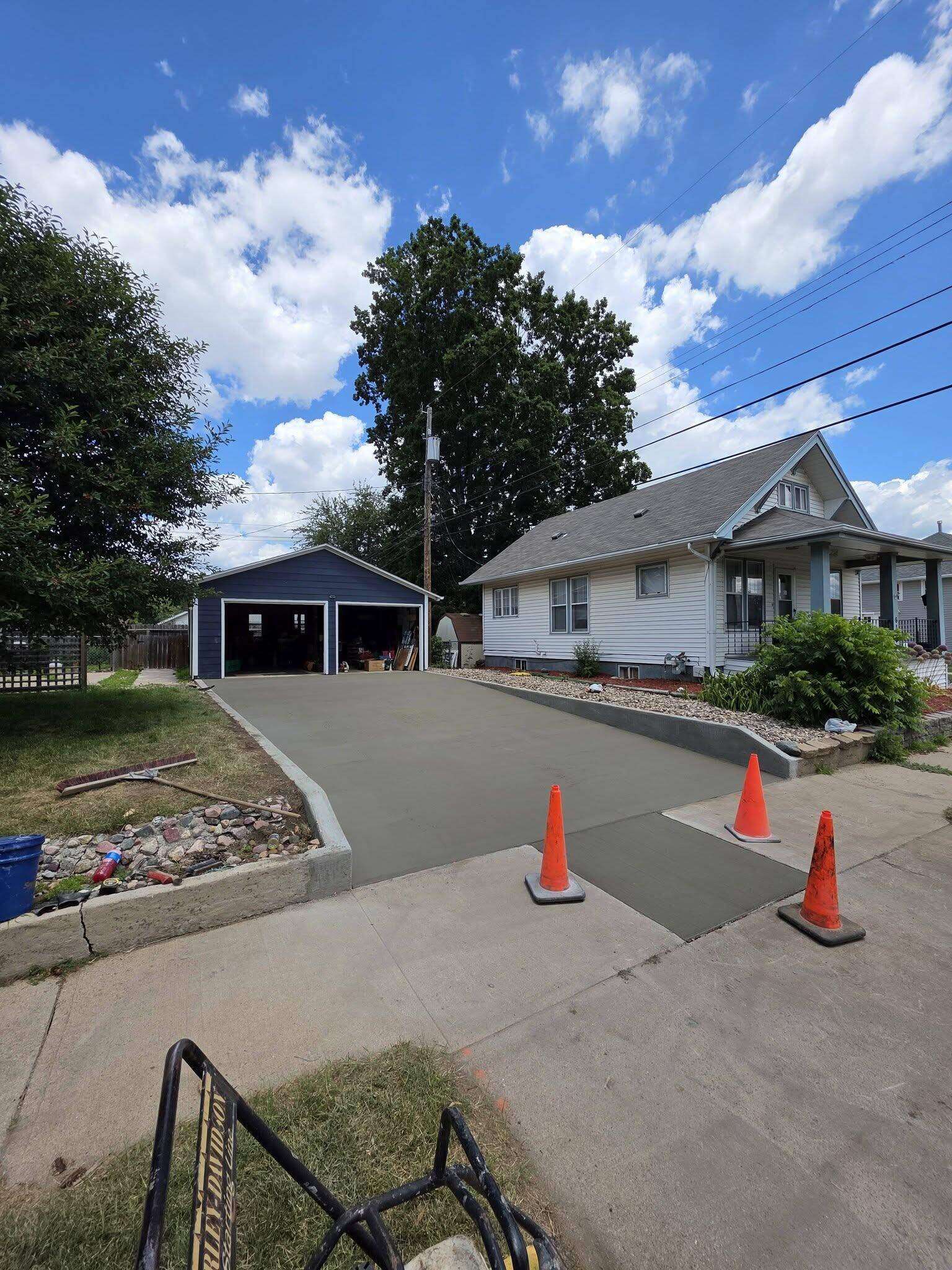 A brand-new dark-gray concrete driveway strip poured against the older, paler walk it replaced