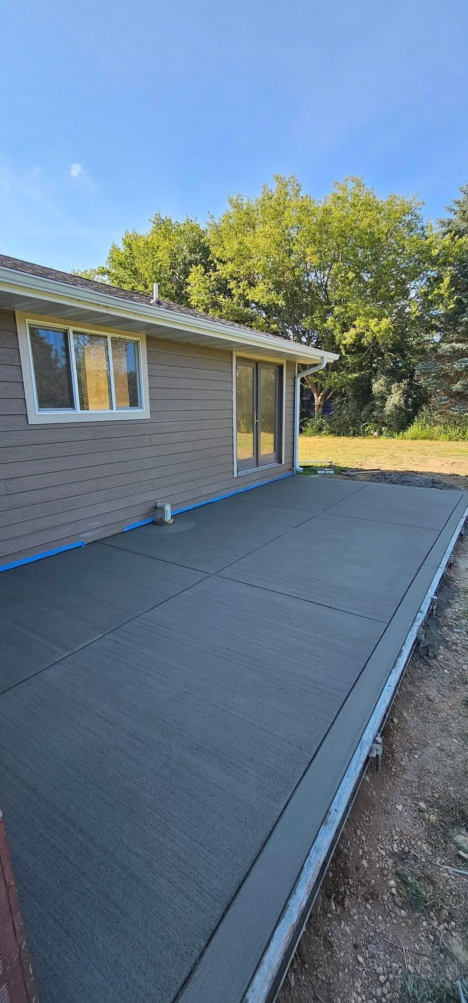 A long broom-finished concrete patio poured along the back of a ranch home, edges cut clean
