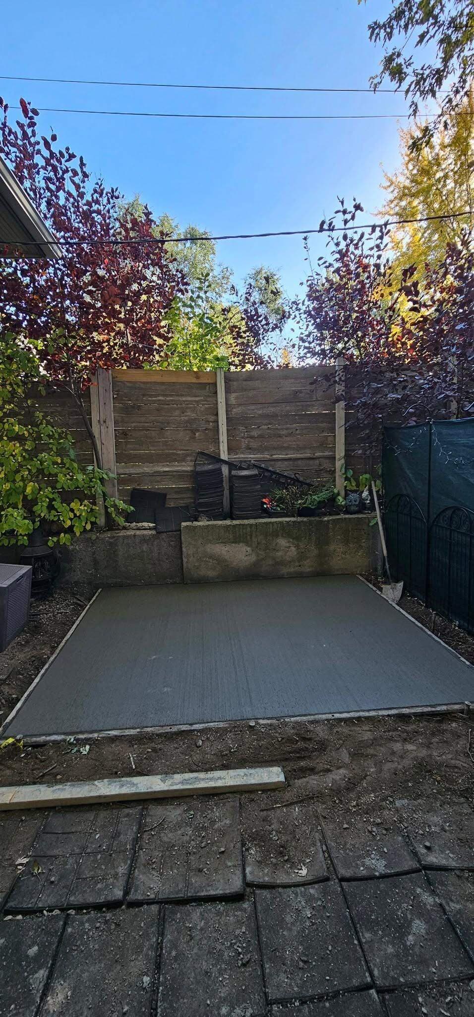 A fresh broom-finished backyard patio poured against a timber retaining wall in fall