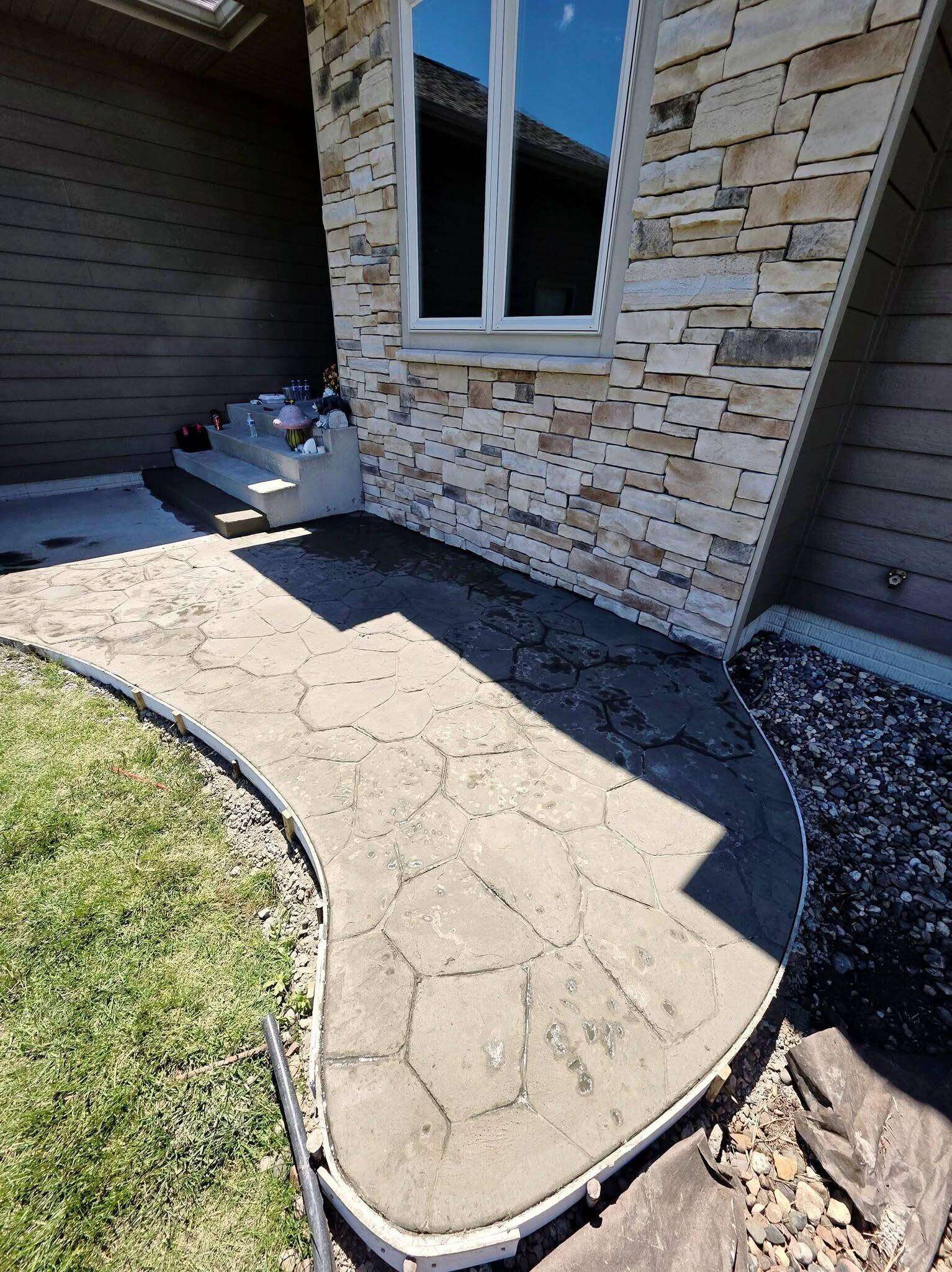A stamped flagstone-pattern concrete walkway curving around the stone corner of a Sioux Falls home