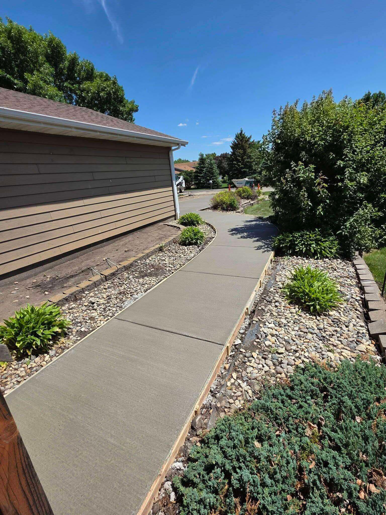 A cured broom-finished walkway running beside a landscaped bed at a Sioux Falls home