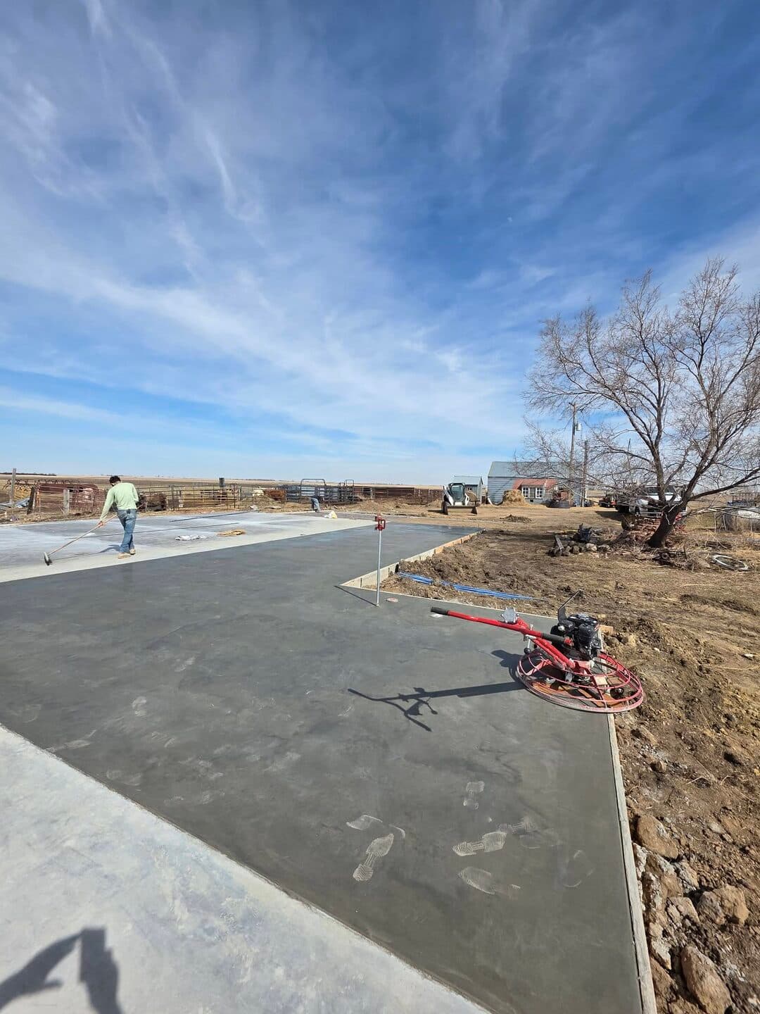 A power trowel staged on a fresh farm pad while my crew floats the far end