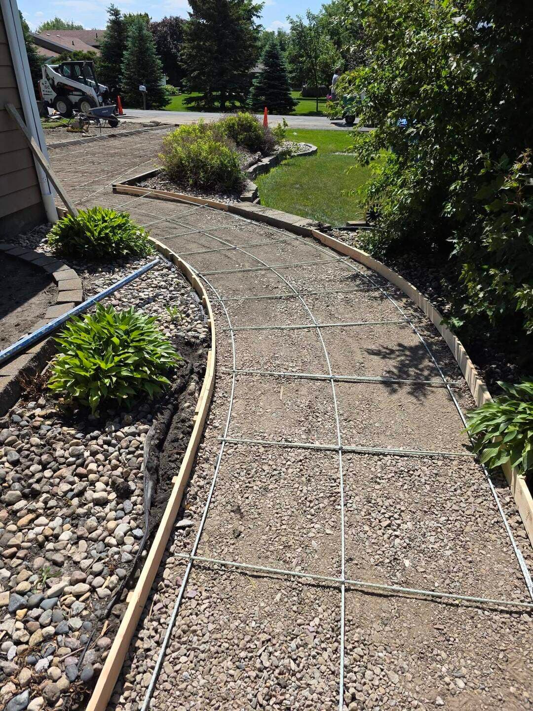 Rebar gridded inside curved walkway forms beside rock landscaping